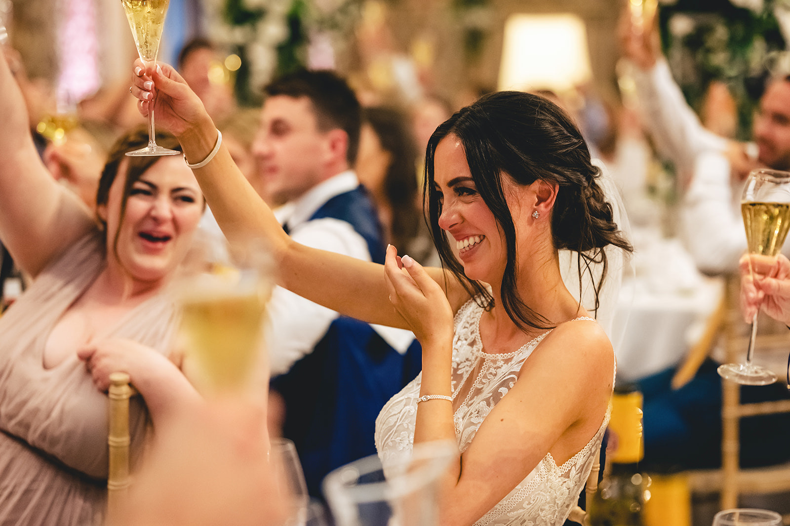 A bride laughing and raising her glass among her wedding guests
