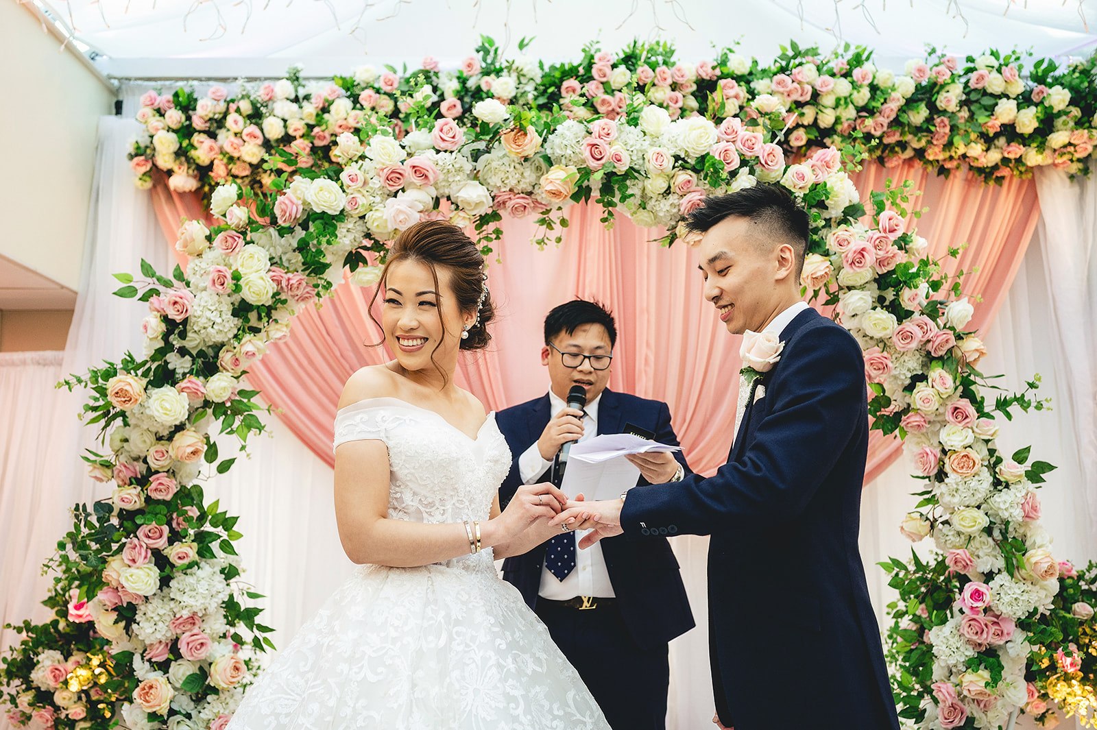 A couple at their ceremony beneath a floral arch